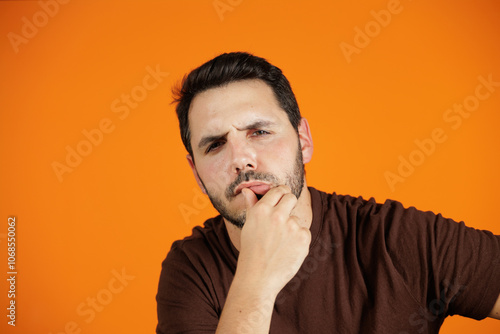 Portrait of young man on orange background. He touches his mouth with his thumb, he is motivated and feeling confident. Man isolated.