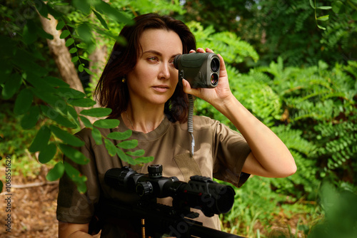 Quadro em tela A woman using a rangefinder in a lush green forest while observing wildlife duri