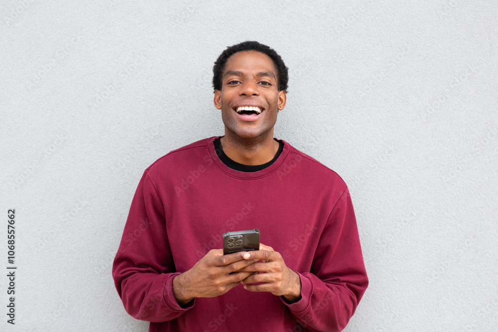 Man smiling while holding a smartphone against a wall Man smiling while holding a smartphone against a wall