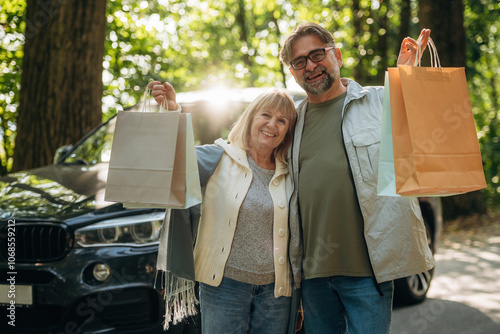 Showing shopping bags, happy. Senior couple together outdoors at nature photo