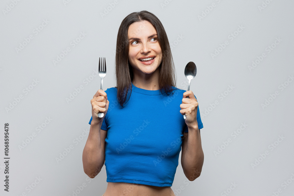 Cheerful young woman with blue top holding spoon and fork, hungry, ready to eat. On white background Cheerful young woman with blue top holding spoon and fork, hungry, ready to eat. On white background