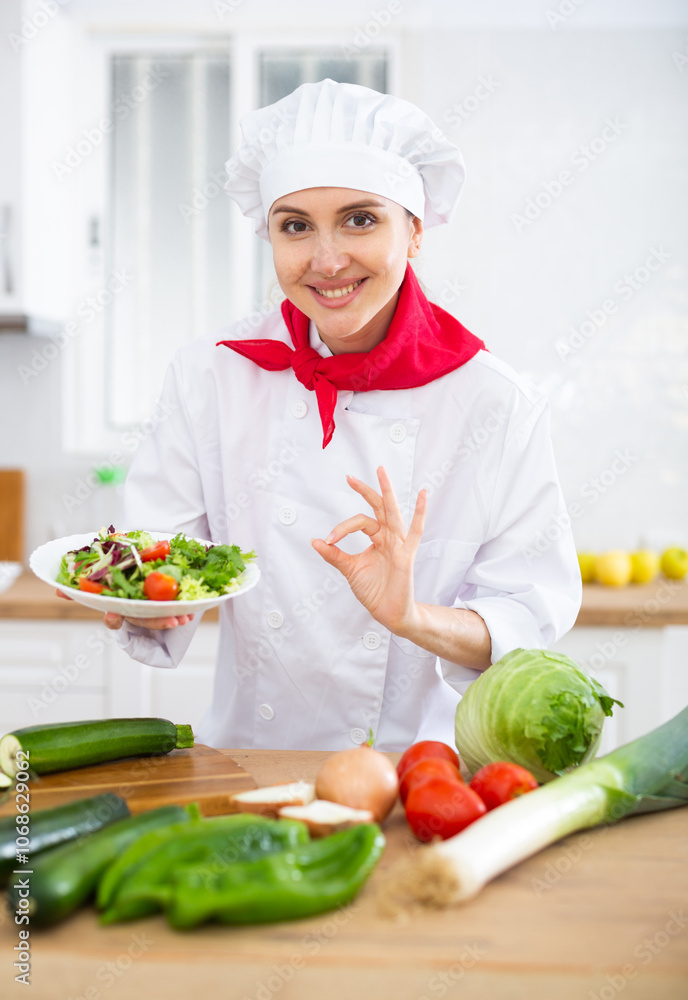 Female chef in white uniform showing approving gesture satisfied with vegetable salad Female chef in white uniform showing approving gesture satisfied with vegetable salad