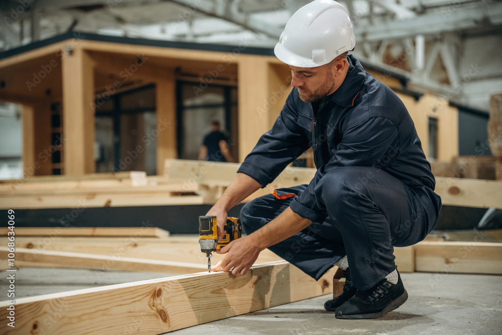 Small drill in hands. Male builder is at construction of wooden house Small drill in hands. Male builder is at construction of wooden house