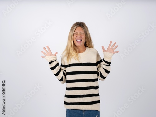 Emotive caucasian teen girl wearing striped knitted sweater over white laughs loudly, hears funny joke or story, raises palms with satisfaction,