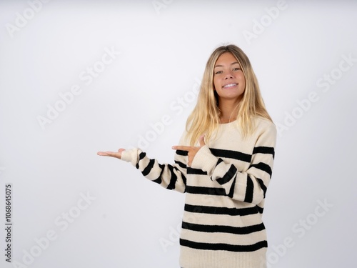 Positive caucasian teen girl wearing striped knitted sweater over white promoter point index finger copyspace hold hand demonstrate offer ads promo