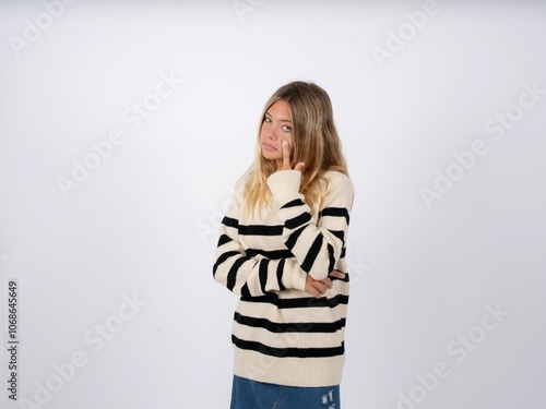 caucasian teen girl wearing striped knitted sweater over white Pointing to the eye watching you gesture, suspicious expression.