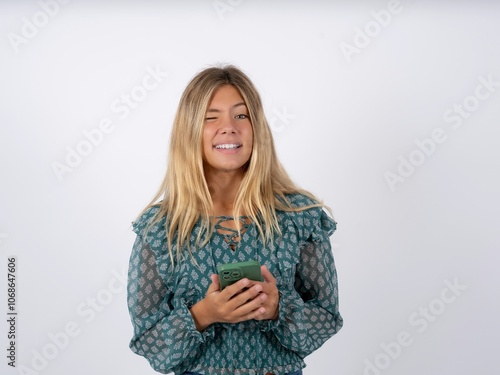 Excited caucasian teen girl wearing green dress over white winking and eye hold smart phone use read social network news