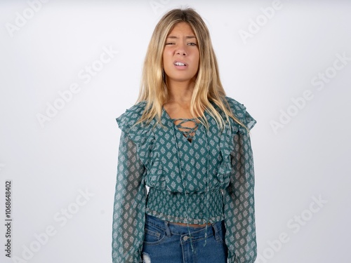 Portrait of dissatisfied caucasian teen girl wearing green dress over white smirks face, purses lips and looks with annoyance at camera, discontent hearing something unpleasant photo