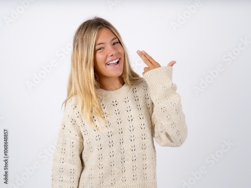 caucasian teen girl wearing knitted sweater over white foolishness around shoots in temple with fingers makes suicide gesture. Funny model makes finger gun pistol photo