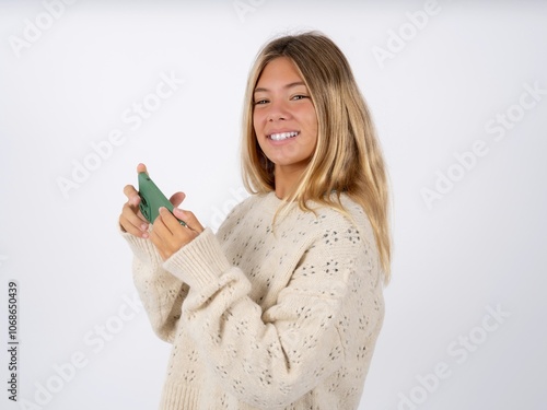 Nice addicted cheerful caucasian teen girl wearing knitted sweater over white using gadget playing network game photo