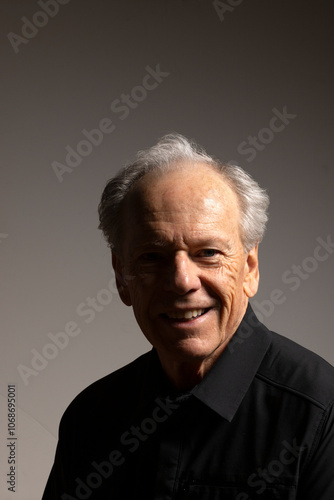 Studio portrait of smiling senior man in black shirt against gray background