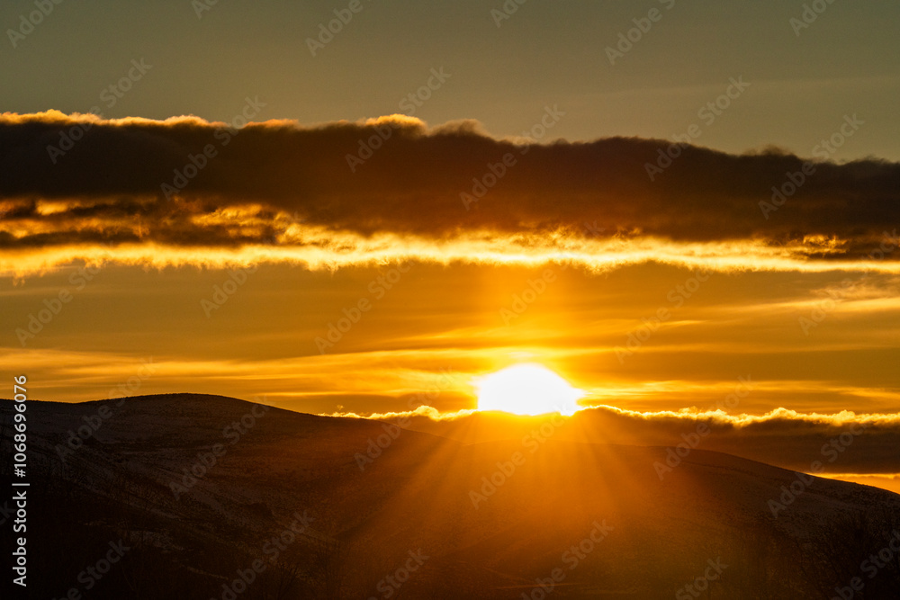Clouds above golden sun setting behind hills Clouds above golden sun setting behind hills