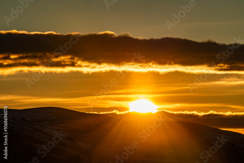 Clouds above golden sun setting behind hills photo