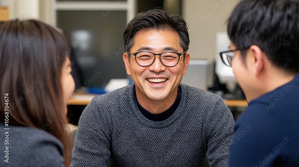 同僚とオフィスで何気ない会話をしている、眼鏡をかけた笑顔の男性 同僚とオフィスで何気ない会話をしている、眼鏡をかけた笑顔の男性