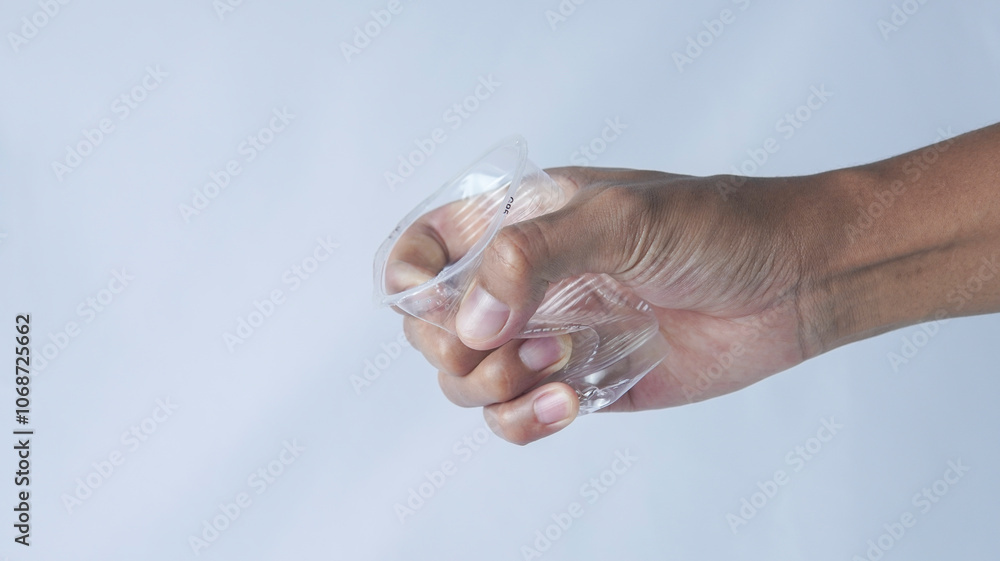 A hand is tightly gripping a small transparent plastic container, squeezing it slightly. The container is partially filled with liquid, showcasing a textured surface against a plain white background A hand is tightly gripping a small transparent plastic container, squeezing it slightly. The container is partially filled with liquid, showcasing a textured surface against a plain white background