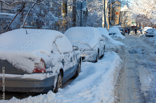 A snowy street with two cars covered in snow photo