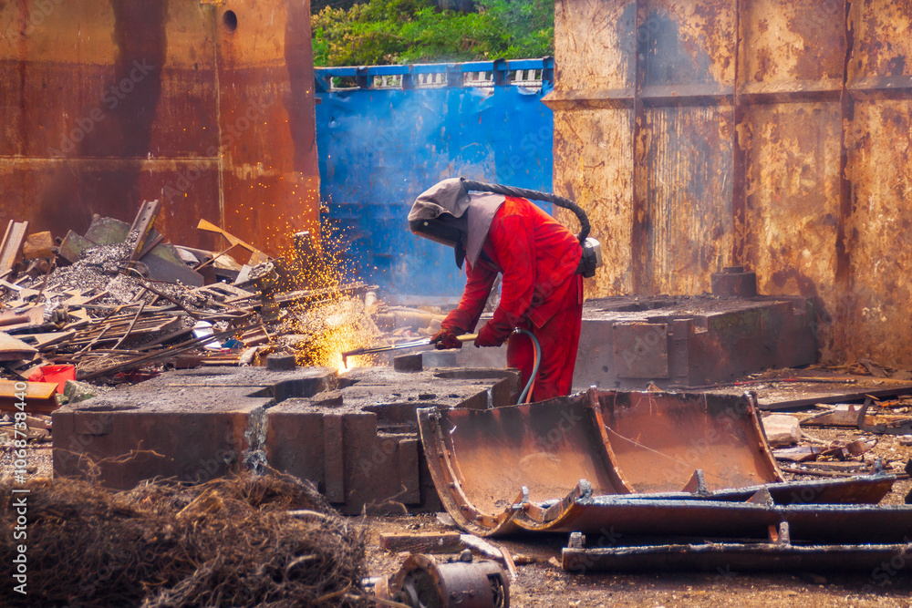 Worker in full protective equipment using gas cutting torch to size steel scrap Worker in full protective equipment using gas cutting torch to size steel scrap