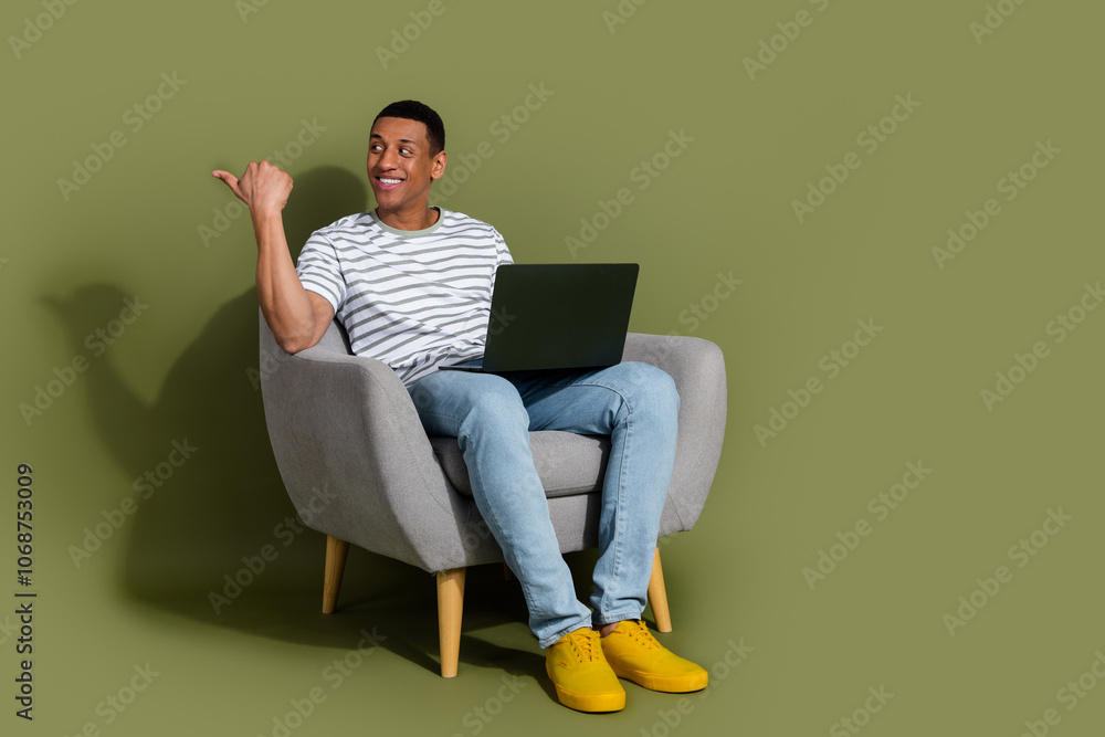 Full length photo of handsome good mood guy wear striped t-shirt texting modern device thumb emtpy space isolated khaki color background Full length photo of handsome good mood guy wear striped t-shirt texting modern device thumb emtpy space isolated khaki color background