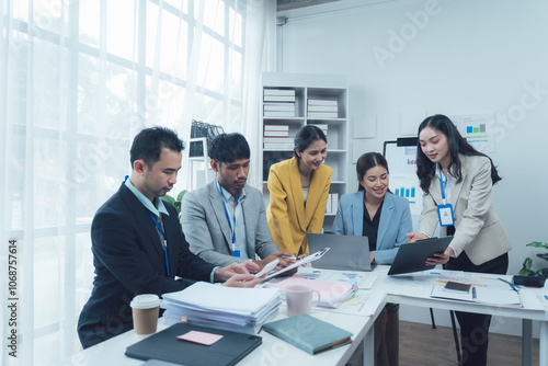 Collaborative Business Meeting: A diverse team of professionals engages in a productive meeting, reviewing documents and using laptops.  The image depicts a modern and collaborative work environment.