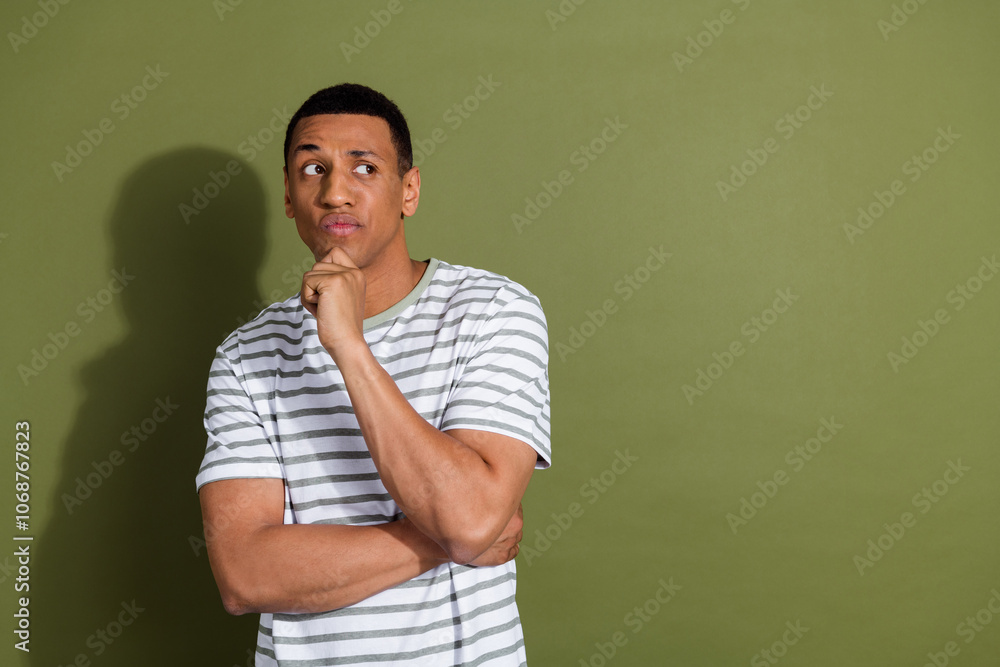 Photo of thoughtful doubtful guy dressed striped t-shirt arm chin looking emtpy space isolated green color background Photo of thoughtful doubtful guy dressed striped t-shirt arm chin looking emtpy space isolated green color background