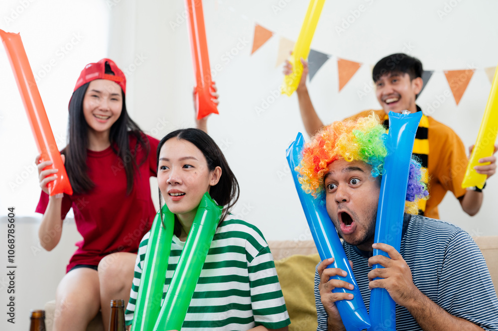 Fototapeta premium A group of Asian male and female friends are excited and happy to watch the World Cup match on TV. and eat snacks together at home Sports fans shout and celebrate the victory of their sports team.