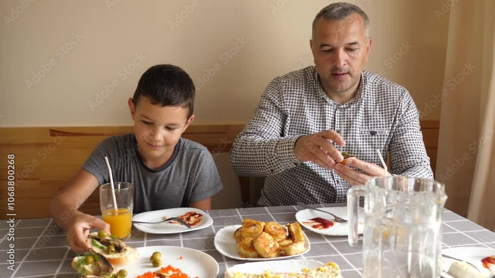 Father and son are sitting at the table, eating food and drinking drinks. Father and son are sitting at the table, eating food and drinking drinks.