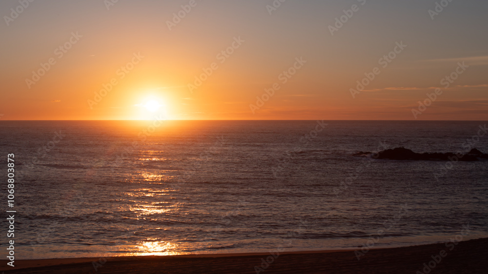 Fototapeta premium Sun dropping below horizon at sunset over the ocean, with sunlight reflected on the waves. Copy space on right.