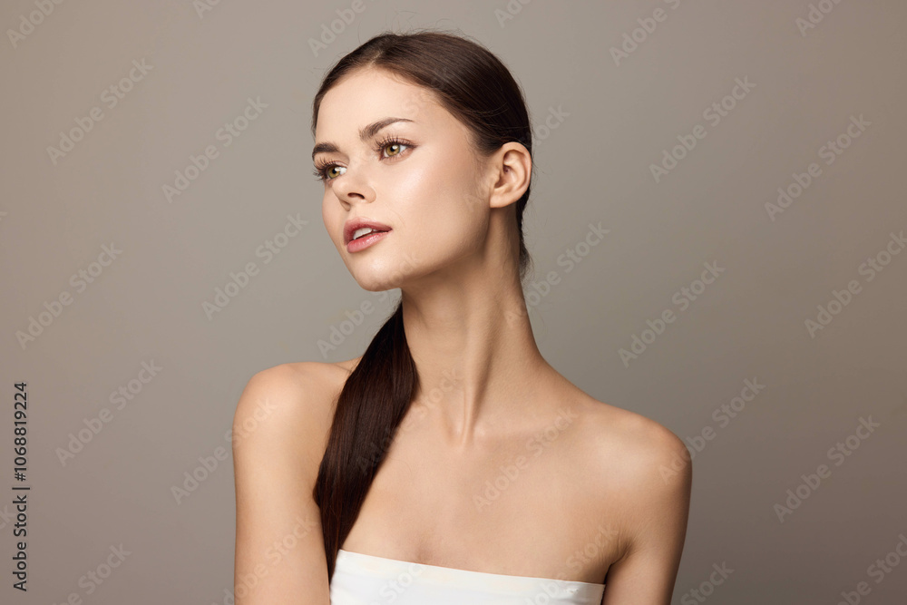 Beautiful young woman with long brown hair posing in front of a gray background with a white towel on her head Beautiful young woman with long brown hair posing in front of a gray background with a white towel on her head