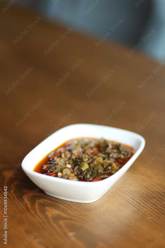A close-up of a traditional Turkish appetizer, közlenmiş biber salçası, served in a white bowl on a wooden table A close-up of a traditional Turkish appetizer, közlenmiş biber salçası, served in a white bowl on a wooden table