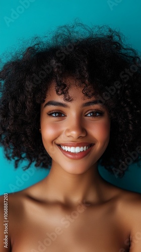 Radiant smile illuminates a portrait of natural beauty, with voluminous curly hair framing a joyful face against a vibrant turquoise background.