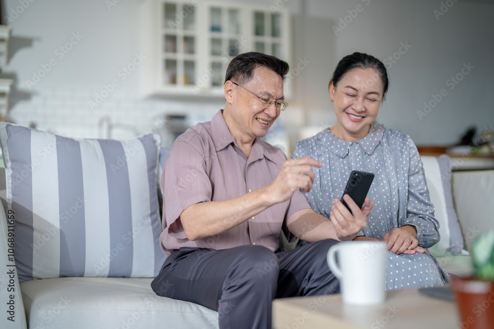 An elderly couple sits together in their cozy living room, smiling and enjoying a moment as they look at something on a smartphone. Their warmth and affection capture a peaceful home atmosphere. An elderly couple sits together in their cozy living room, smiling and enjoying a moment as they look at something on a smartphone. Their warmth and affection capture a peaceful home atmosphere.