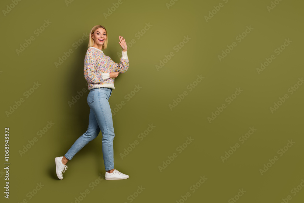 Joyful young woman in casual sweater and jeans waving energetically on khaki background, promoting cheerful style and positive energy Joyful young woman in casual sweater and jeans waving energetically on khaki background, promoting cheerful style and positive energy