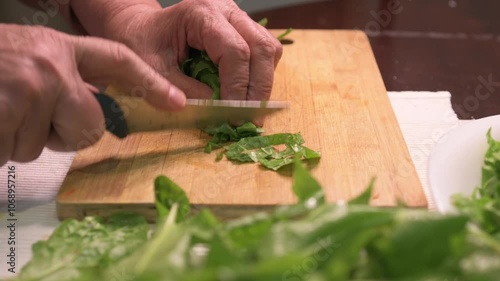 An elderly woman cutting sorrel on a cutting board. 