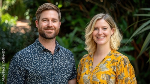 Caucasian american man and woman are smiling for the camera. The man is wearing a blue shirt with a pattern and the woman is wearing a yellow dress