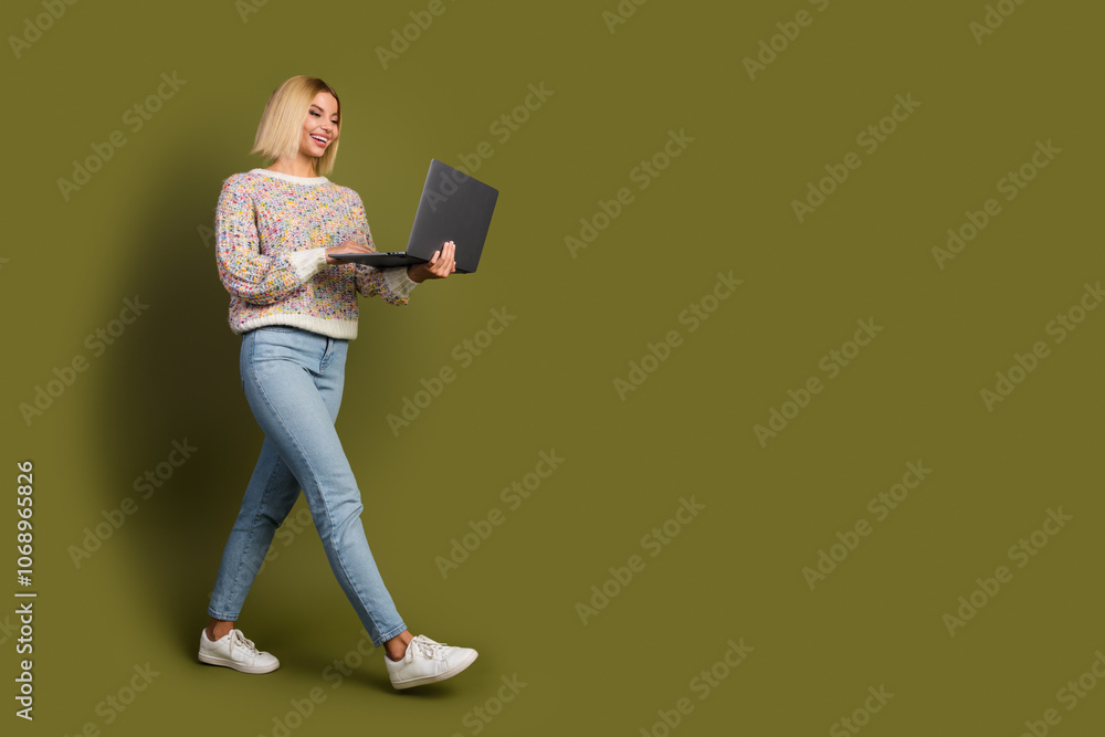 Young woman in colorful sweater using laptop against khaki background for online shopping and promotion concepts Young woman in colorful sweater using laptop against khaki background for online shopping and promotion concepts