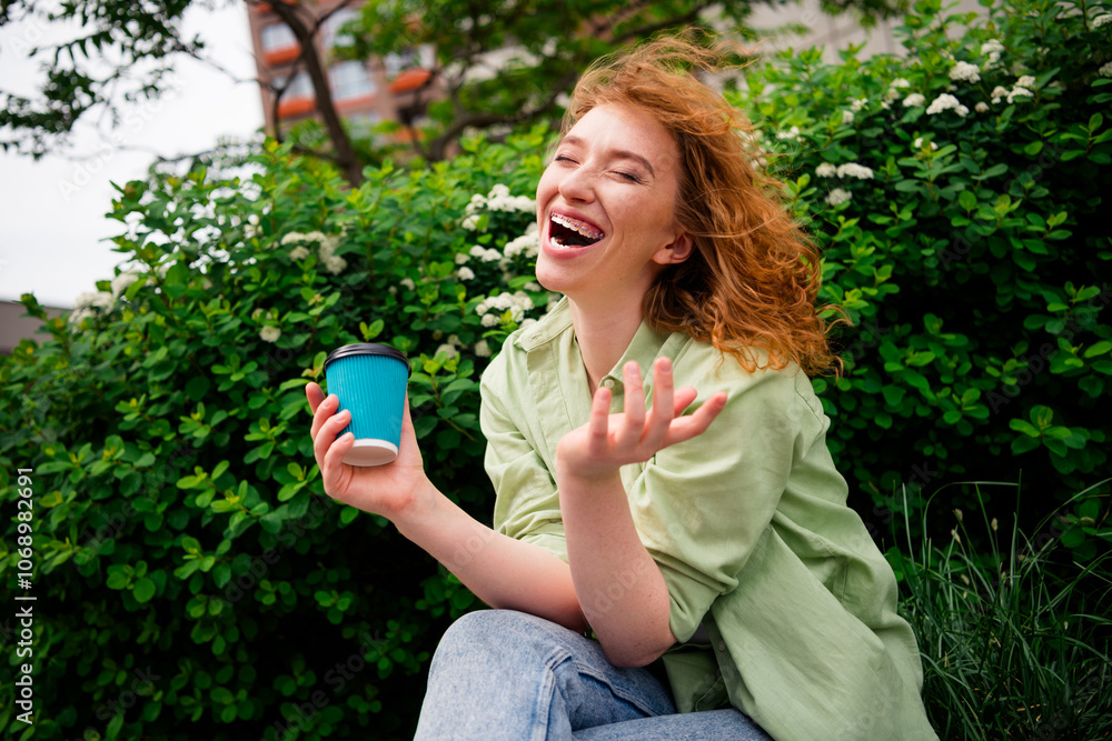 Joyful young redhaired woman enjoying a sunny day outdoors holding coffee and laughing in natural light Joyful young redhaired woman enjoying a sunny day outdoors holding coffee and laughing in natural light