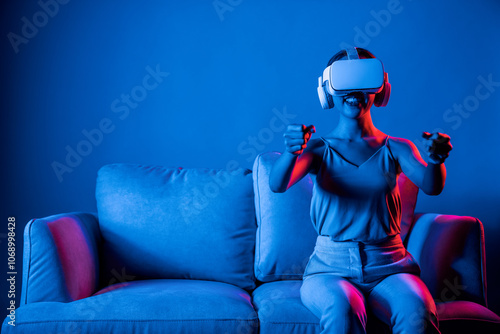 Smart Female sitting on sofa surrounded by neon light wear VR headset connecting metaverse, futuristic cyberspace community technology. Elegant woman play car racing game of VRX world. Hallucination. photo