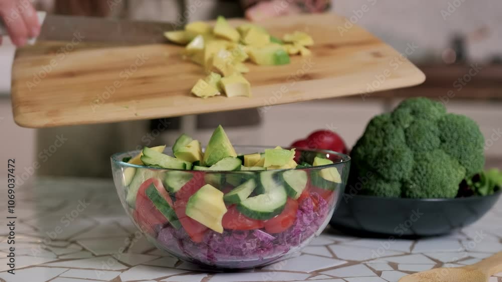 Chef adds freshly sliced avocado to a glass bowl of colorful salad ingredients Chef adds freshly sliced avocado to a glass bowl of colorful salad ingredients