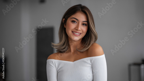 A young South Asian woman with long, wavy hair smiles warmly at the camera, showcasing her natural beauty in a soft-lit studio setting.