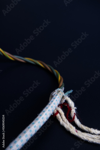 Old electrical wire on black background in vertical. Close-up wire covering peeled because it's old and broken and needs to be repaired. Concept of household item, fibers, wiring, energy, and power. photo