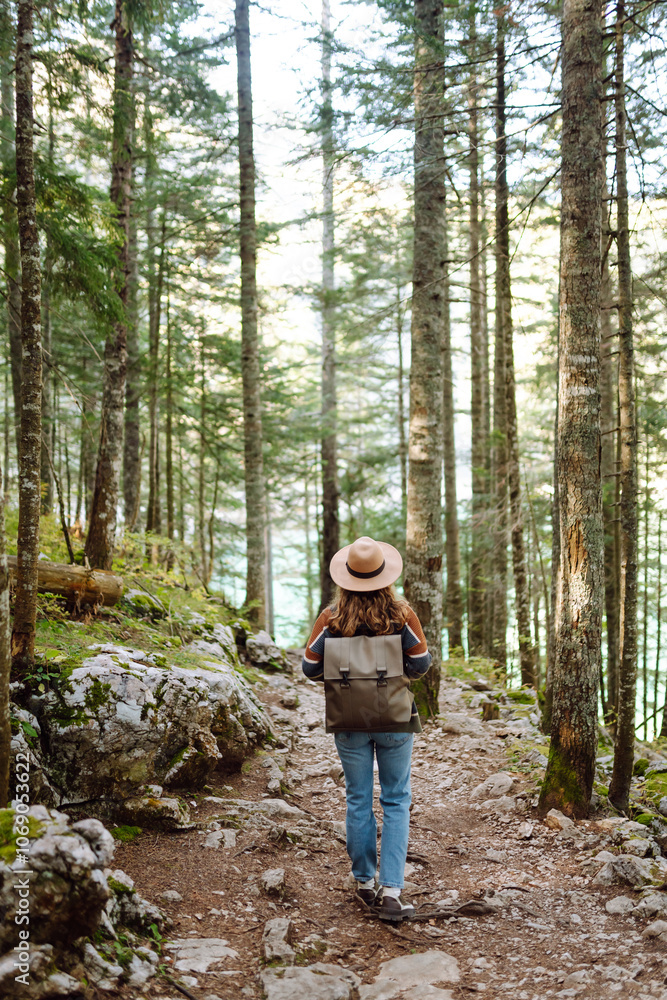 Woman in hat with backpack walks along ground road in dense forest. Fresh air and wild nature. Hiking. Woman in hat with backpack walks along ground road in dense forest. Fresh air and wild nature. Hiking.