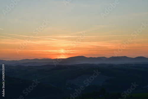 Obraz na płótnie The orange sunset and its rays dazzle the green forests and meadows w salonie