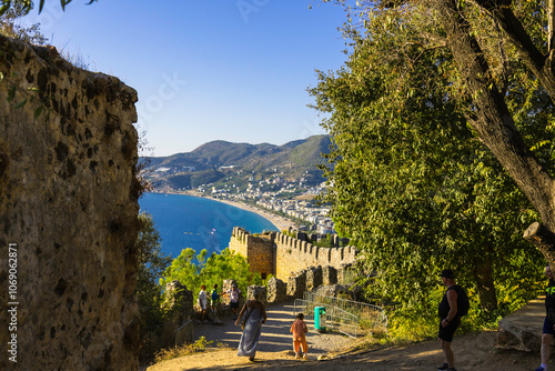 Fototapeta Naklejka Na Ścianę i Meble -  Alanya castle top view on the mountain with coast ferry boat on blue sea . Beautiful cleopatra beach Alanya Turkey landscape travel landmark.