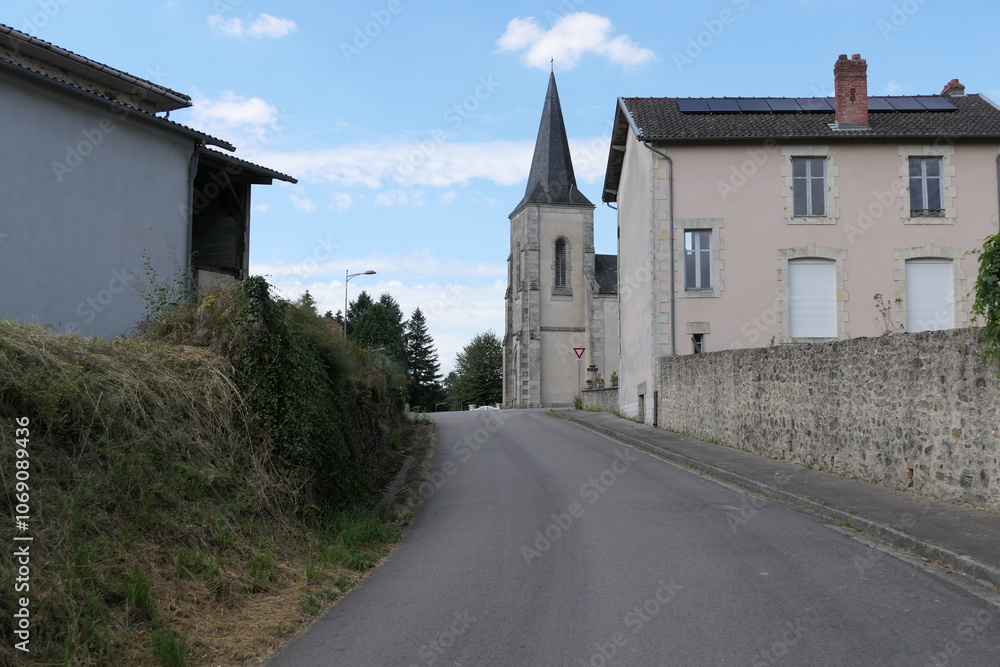 A quaint church tower rises on the edge of a narrow, French road, framed by stone walls and shaded by nearby trees. A quaint church tower rises on the edge of a narrow, French road, framed by stone walls and shaded by nearby trees.
