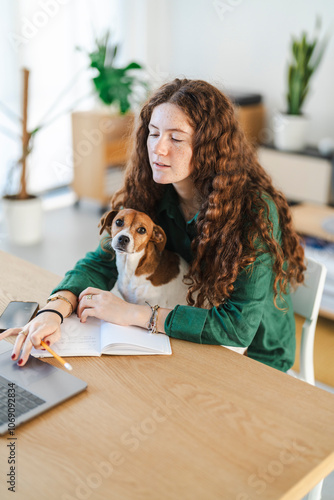 Young woman working at her desk with her dog on her lap in a casual workspace photo