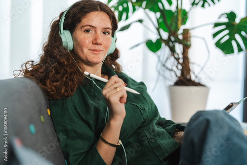 Young woman holding a tablet and looking content in a bright room filled with green plants photo