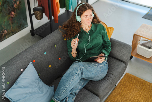 Woman lounging on a couch with headphones on, enjoying her tablet in a cozy, colorful living space photo