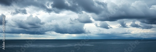 A vast, blue sky filled with fluffy white clouds hangs over a calm, ocean horizon