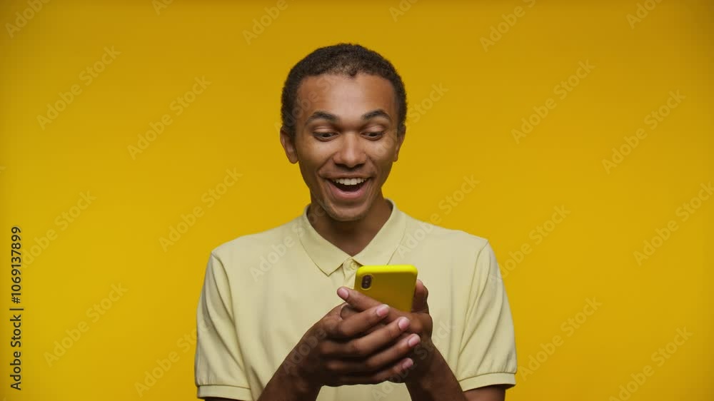 Excited Man Reacting to Smartphone Against Yellow Background Excited Man Reacting to Smartphone Against Yellow Background