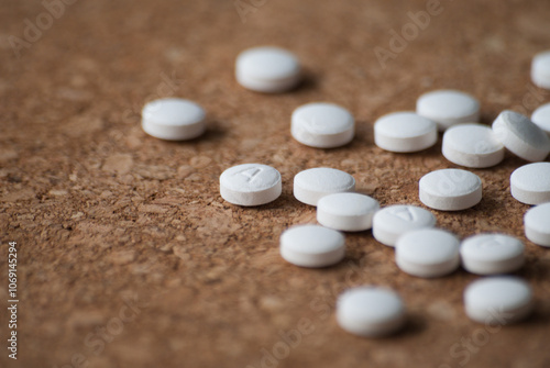 A pile of round white pills on a wooden background. The pills are scattered on the surface.